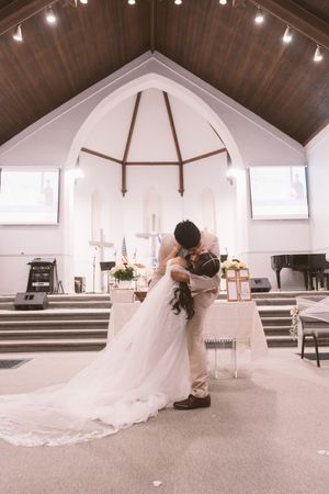 Bride and groom share a romantic kiss at the altar of a white church with wooden beam ceiling.