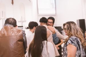 Group of people sharing a warm embrace during a church gathering in a bright white chapel setting.