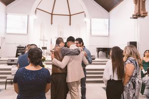 Group of people praying together in a white church, gathered in a circle with hands raised in worship.