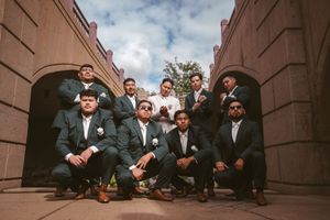 Group of groomsmen in navy suits with boutonnieres posing confidently outdoors at a wedding venue.