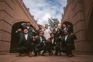 Groom in white suit posing with groomsmen in black suits under stone arches.