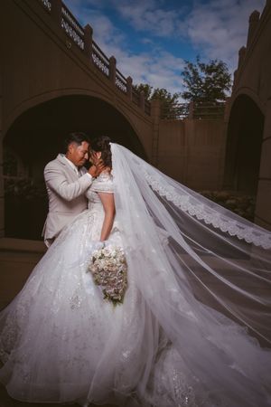 Newlyweds sharing romantic moment under stone arch with billowing lace wedding veil.