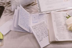 Open Bible and handwritten notes on a table with white flowers at a religious ceremony.