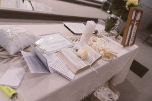 Wedding ceremony table with open Bible, white roses, candles, and elegant decorations on a white linen tablecloth.