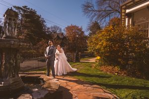 Bride and groom pose together in a sunlit garden with autumn foliage and historic estate backdrop.
