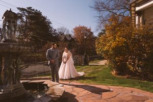 Bride and groom share a moment by a stone fountain surrounded by fall foliage at an elegant estate.