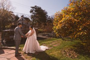Bride and groom hold hands in autumn garden with colorful fall foliage at outdoor wedding.