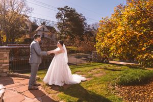 Bride and groom hold hands in a sunlit autumn garden, bride wearing a white ball gown with a long train.
