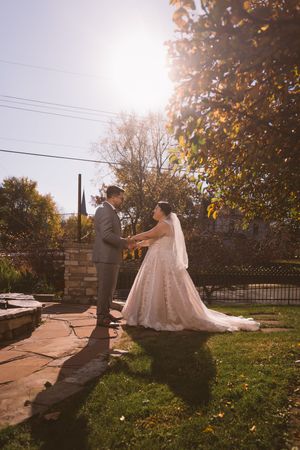Bride and groom holding hands outdoors in golden sunlight, bride in flowing white gown with veil on stone patio.