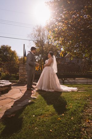 Bride and groom share a romantic moment outdoors in golden sunlight, surrounded by autumn trees and lush green grass.