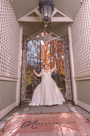 Bride in lace gown stands in ornate iron gateway at Rivertown Inn during autumn wedding celebration.