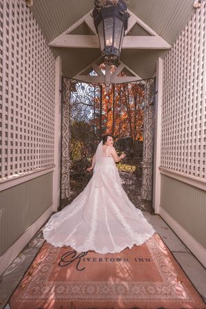 Bride in a stunning white ballgown with long train stands at ornate iron gates of Rivertown Inn.