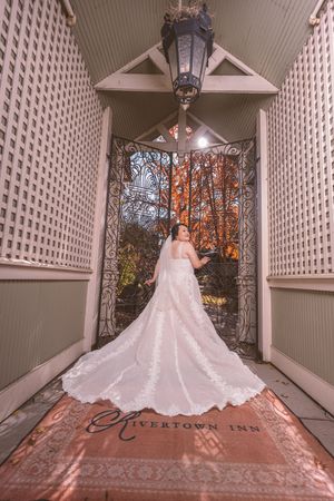 Bride in lace gown with long train poses at ornate iron gate of Rivertown Inn wedding venue.