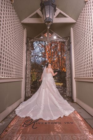 Bride in lace gown poses at ornate iron gate entrance of the elegant Rivertown Inn wedding venue.