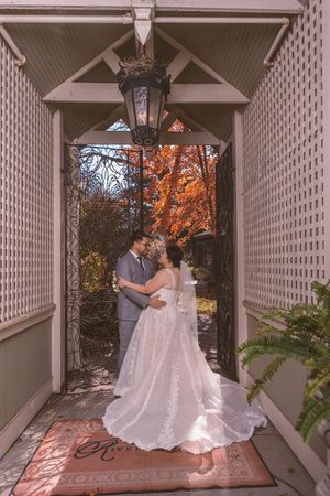 Bride and groom share romantic moment under lantern archway with vibrant autumn foliage backdrop.