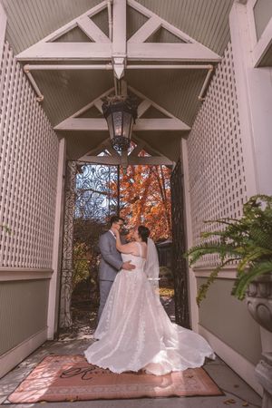 Bride and groom share a romantic moment under a lantern-lit pergola with vibrant fall foliage backdrop.