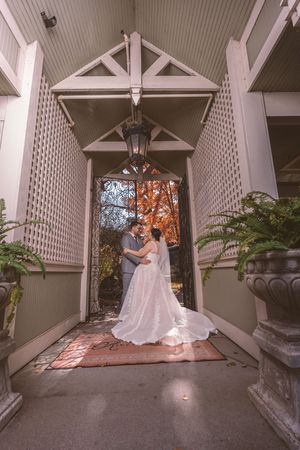 Bride and groom embrace romantically in a charming latticed porch entrance with autumn foliage behind.