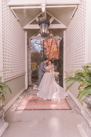 Bride and groom share a romantic embrace in a white lattice entryway with autumn foliage and a hanging lantern.