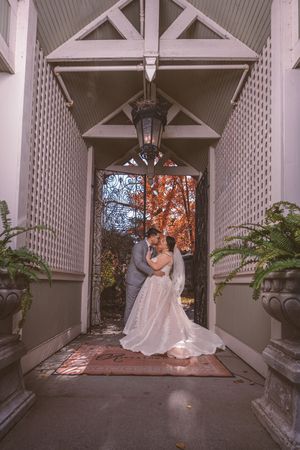 Bride and groom share a romantic kiss under an elegant covered entrance with autumn foliage and hanging lantern.