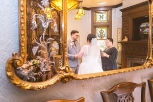 Wedding ceremony reflected in ornate gold mirror as officiant guides bride and groom through vows.