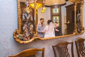 Bride and groom share a first look moment reflected in an ornate gold-framed mirror indoors.