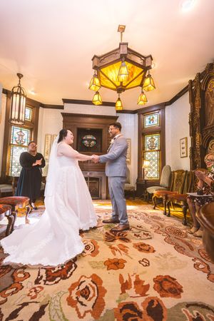 Bride and groom share a first look moment in an ornate Victorian room with stained glass windows.