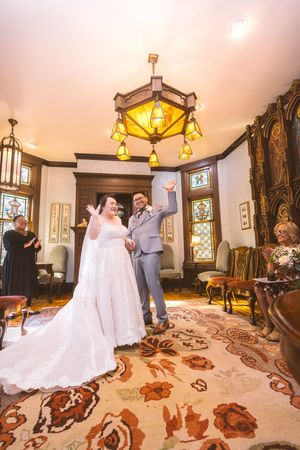 Joyful bride and groom celebrate their wedding ceremony in a vintage room with stained glass windows.