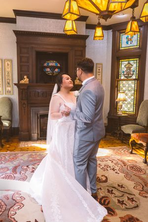 Bride and groom share first dance in elegant Victorian room with stained glass windows and fireplace.