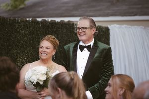 Smiling bride and groom in green velvet tuxedo at outdoor wedding ceremony near waterfall.