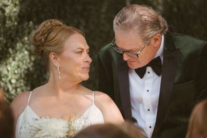 Bride and older groom in black tuxedo share an intimate glance during outdoor wedding ceremony.