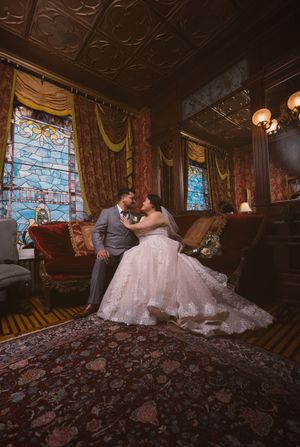 Bride and groom share an intimate moment in a Victorian room with stained glass windows and ornate decor.