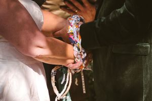 Close-up of bride and groom performing colorful handfasting ceremony ritual with decorative braided cord.