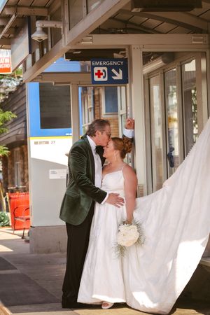 Bride and groom share a kiss outside an emergency entrance, her veil flowing in the breeze.
