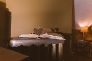 Open book with pages folded into a heart shape on a wooden table in a warmly lit cozy room.