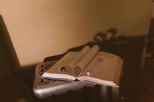 An open book with rolled pages resting on an ornate wooden stand in warm, soft lighting.
