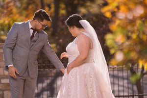 Groom in gray suit admires bride in lace gown against a backdrop of golden autumn foliage.