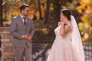 Groom in gray suit smiles at bride in lace wedding gown during outdoor fall first look.