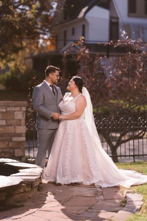 Bride and groom share a romantic moment outdoors on a stone patio with autumn foliage backdrop.