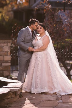 Bride in lace gown and groom in gray suit share a romantic moment outdoors on stone steps at fall wedding.