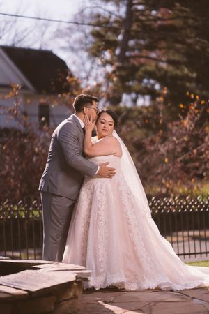 Groom in gray suit whispering to bride in lace ball gown outdoors during fall wedding portrait.