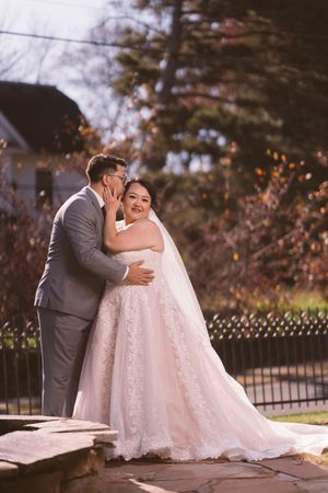 Bride and groom share a romantic outdoor moment, groom whispering to smiling bride in lace wedding gown.