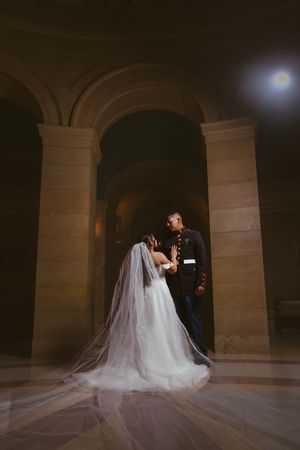 Marine groom and bride share romantic moment under stone archway in dramatic wedding portrait.