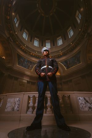 US Marine stands at attention in dress uniform inside grand domed rotunda building.