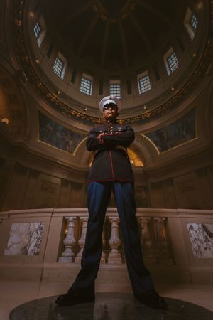 US Marine in dress uniform stands confidently with arms crossed inside an ornate domed rotunda.