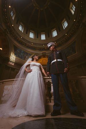 Marine groom in dress blues and bride in white gown pose under stunning rotunda dome for wedding portrait.