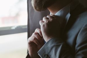 Man in gray suit adjusting his tie near a window, getting dressed for a formal event or business meeting.