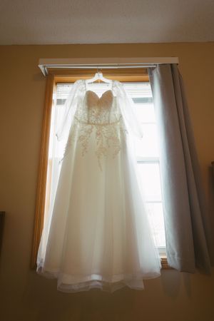 Elegant strapless lace ball gown wedding dress hanging in window on hanger before bridal ceremony.