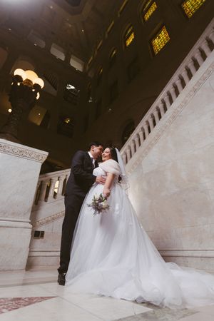 Bride and groom share a romantic moment on marble stairs in an elegant grand hall wedding venue.