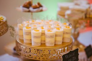 Wedding dessert table featuring rows of layered peach panna cotta cups on a gold cake stand.