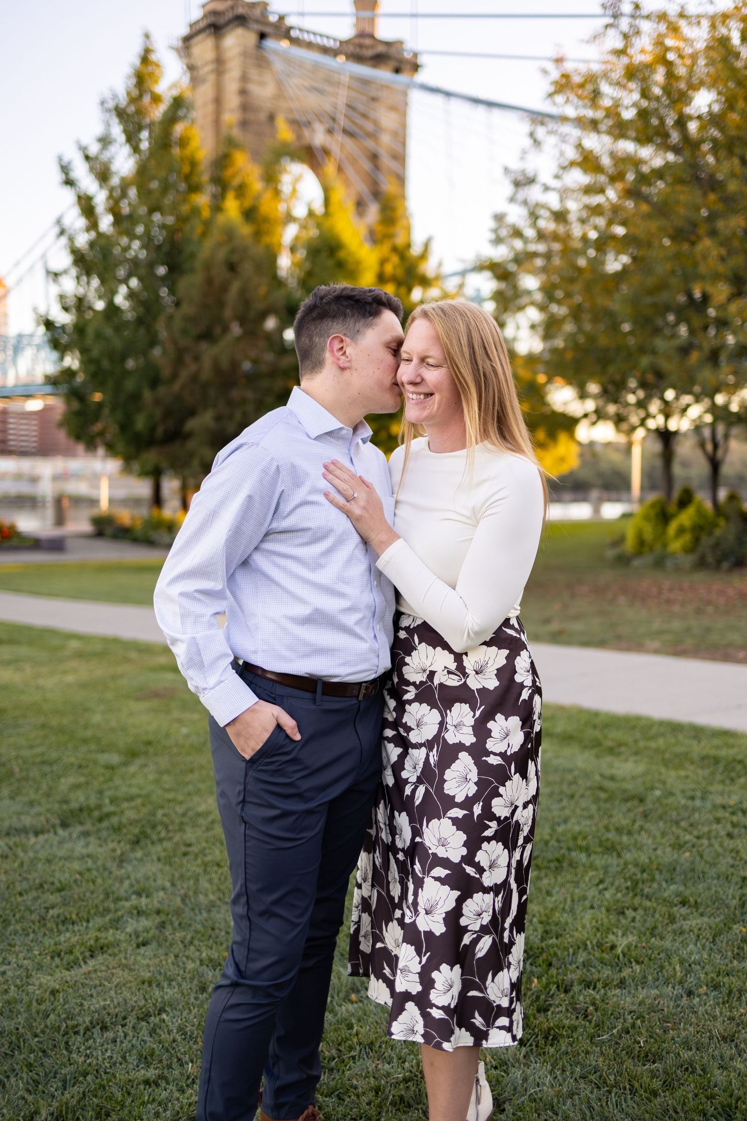 Couple kissing on a bridge in Smale Park in Cincinnati while showing off an engagement ring during their fall engagement photoshoot.